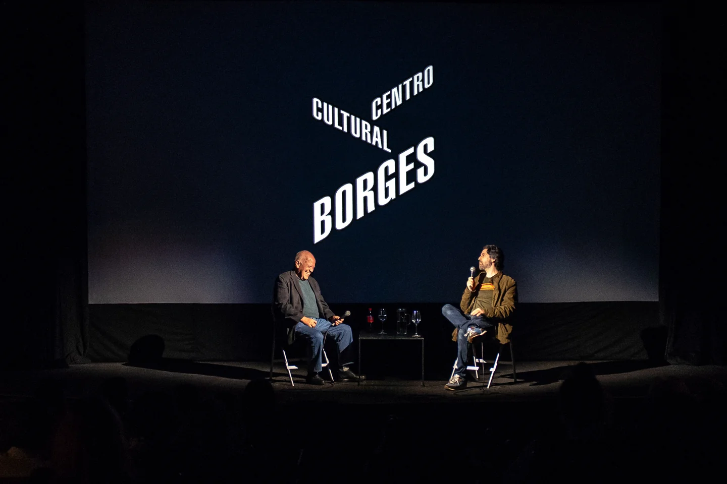 Dos personas en un escenario ante una proyección del Centro Cultural Borges