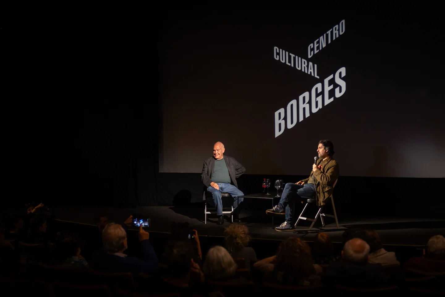 Dos personas conversando con micrófonos ante público en el Centro Cultural Borges