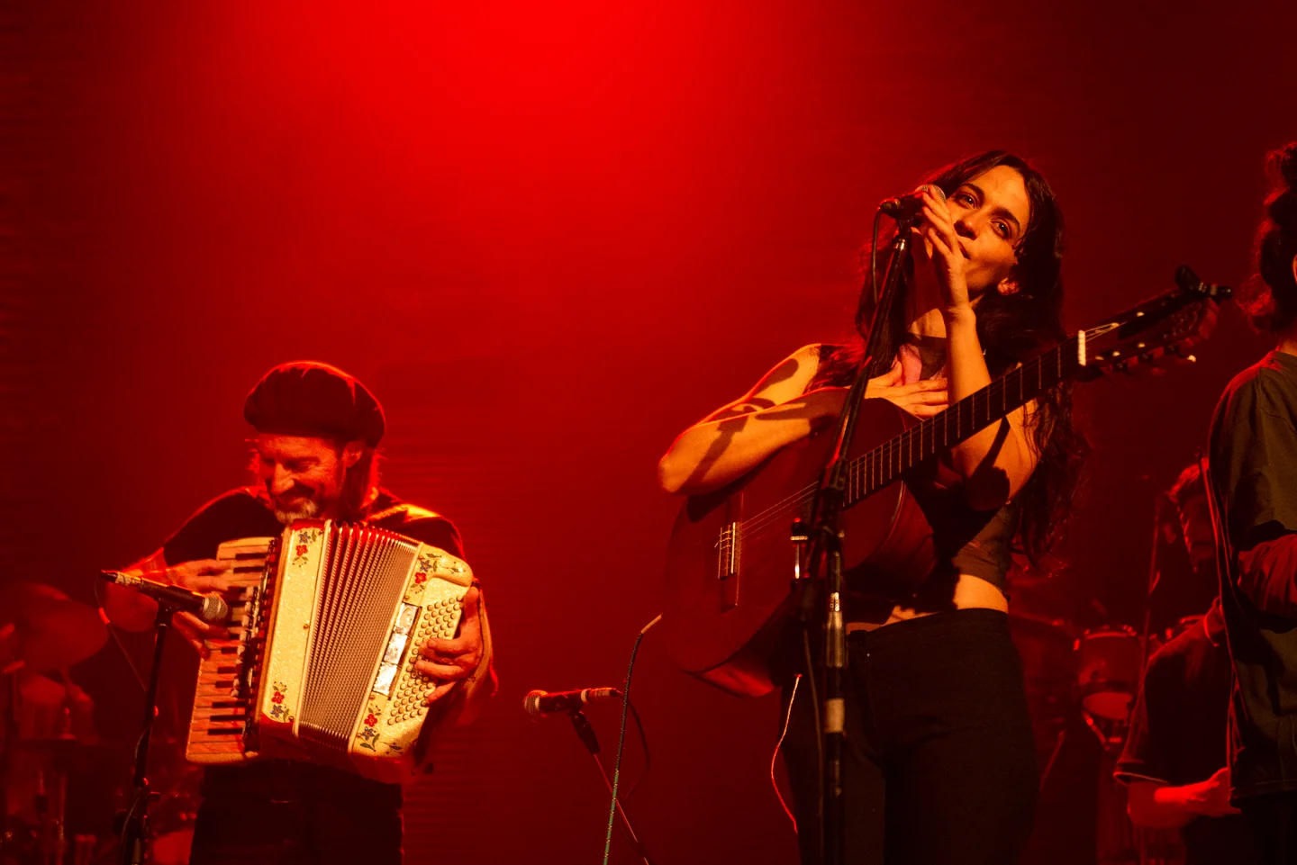 Acordeonista y cantante con guitarra durante un concierto bajo iluminación roja