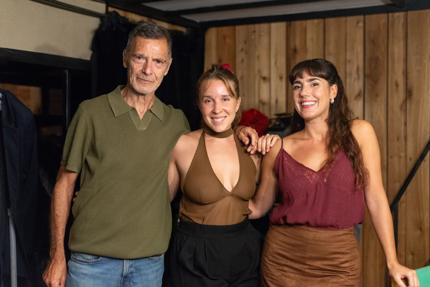Tres personas posando juntas ante una pared de madera