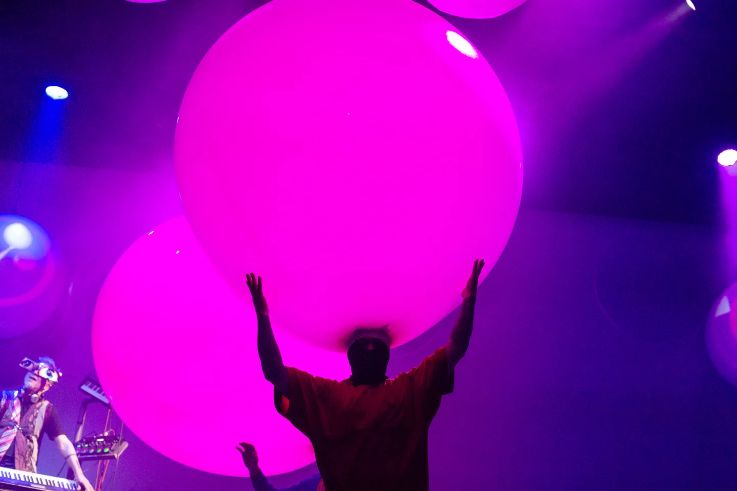Silueta con los brazos elevados bajo una gran esfera rosa en un escenario iluminado