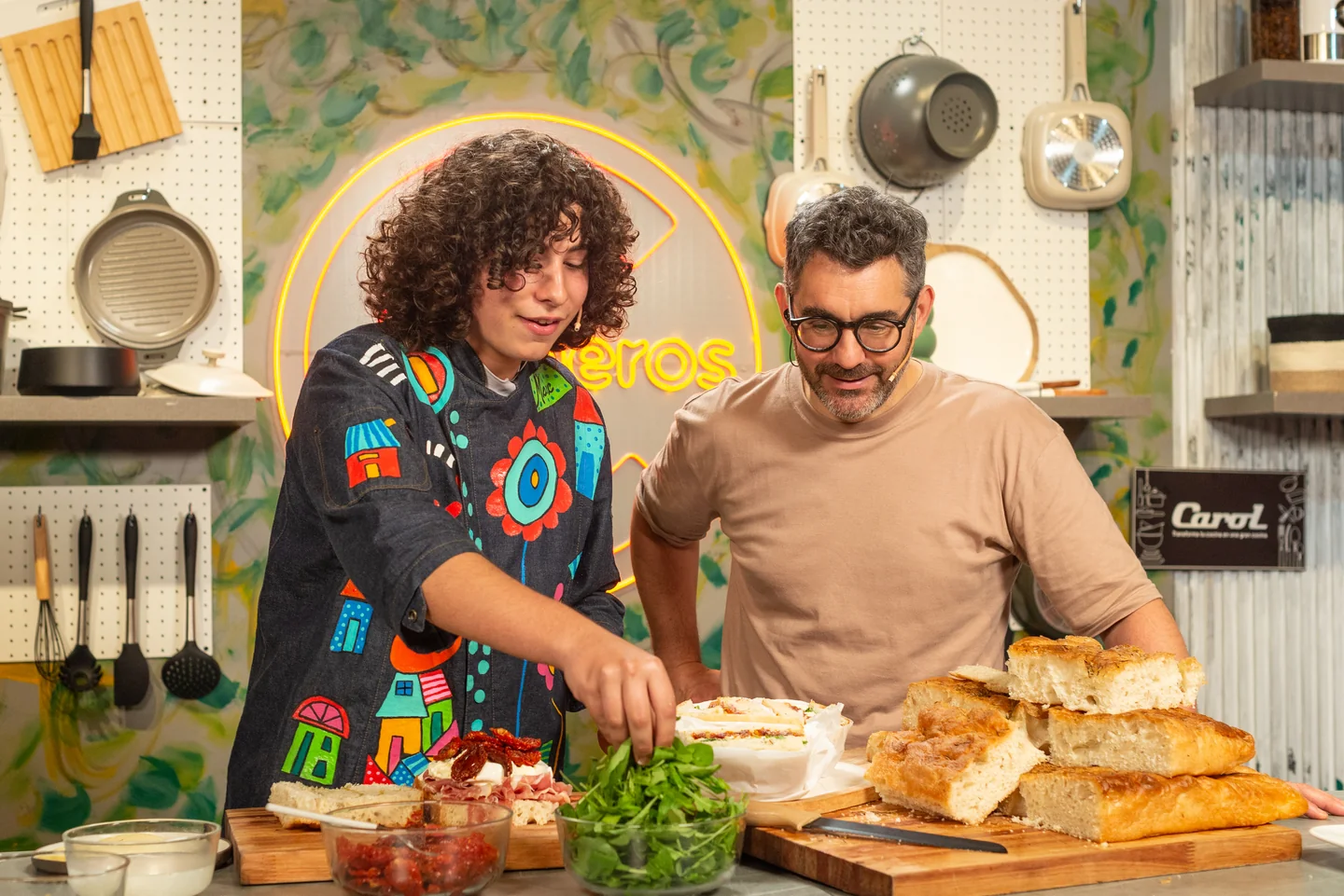 Dos personas preparando alimentos sobre una mesada en un set de cocina