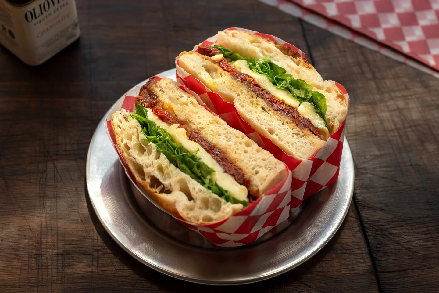 Sándwich cortado con hojas verdes sobre papel cuadriculado en un plato metálico