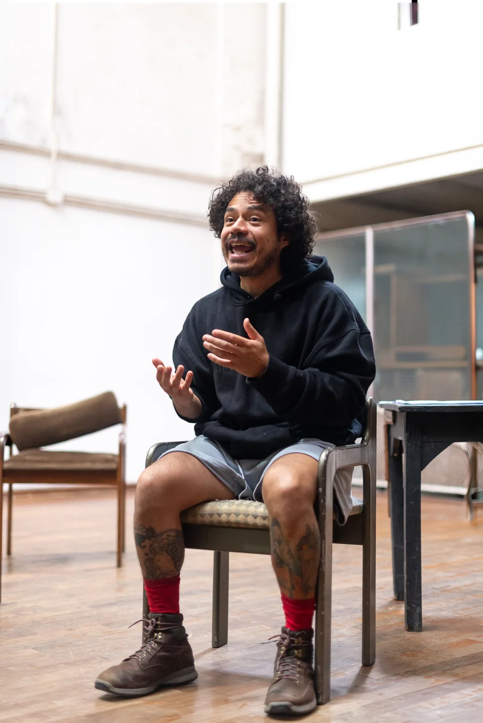 Persona sentada con buzo negro y pantalón corto, sonriendo y gesticulando
