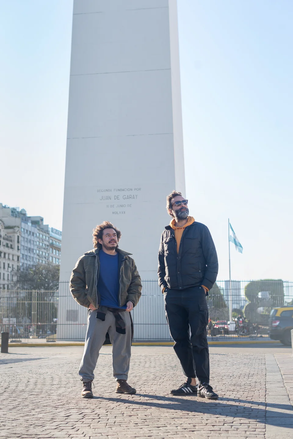 Dos personas junto a un monumento alto en una plaza urbana