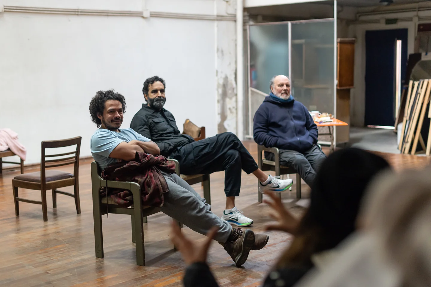 Tres personas sentadas durante un encuentro en una sala, con público en primer plano